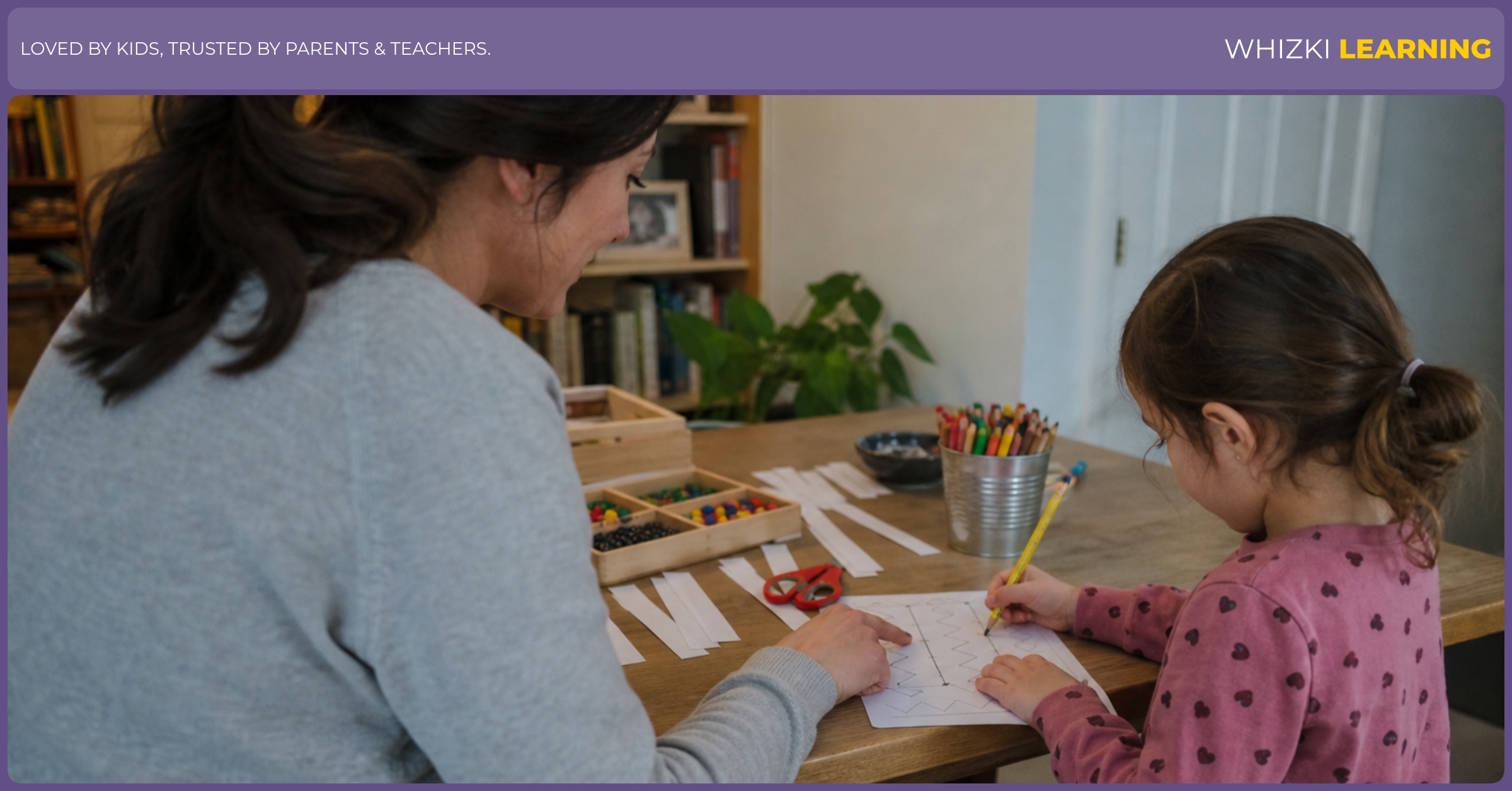 A parent sits beside a child who traces, cuts, sorts, and draws with paper materials at a warm kitchen table.