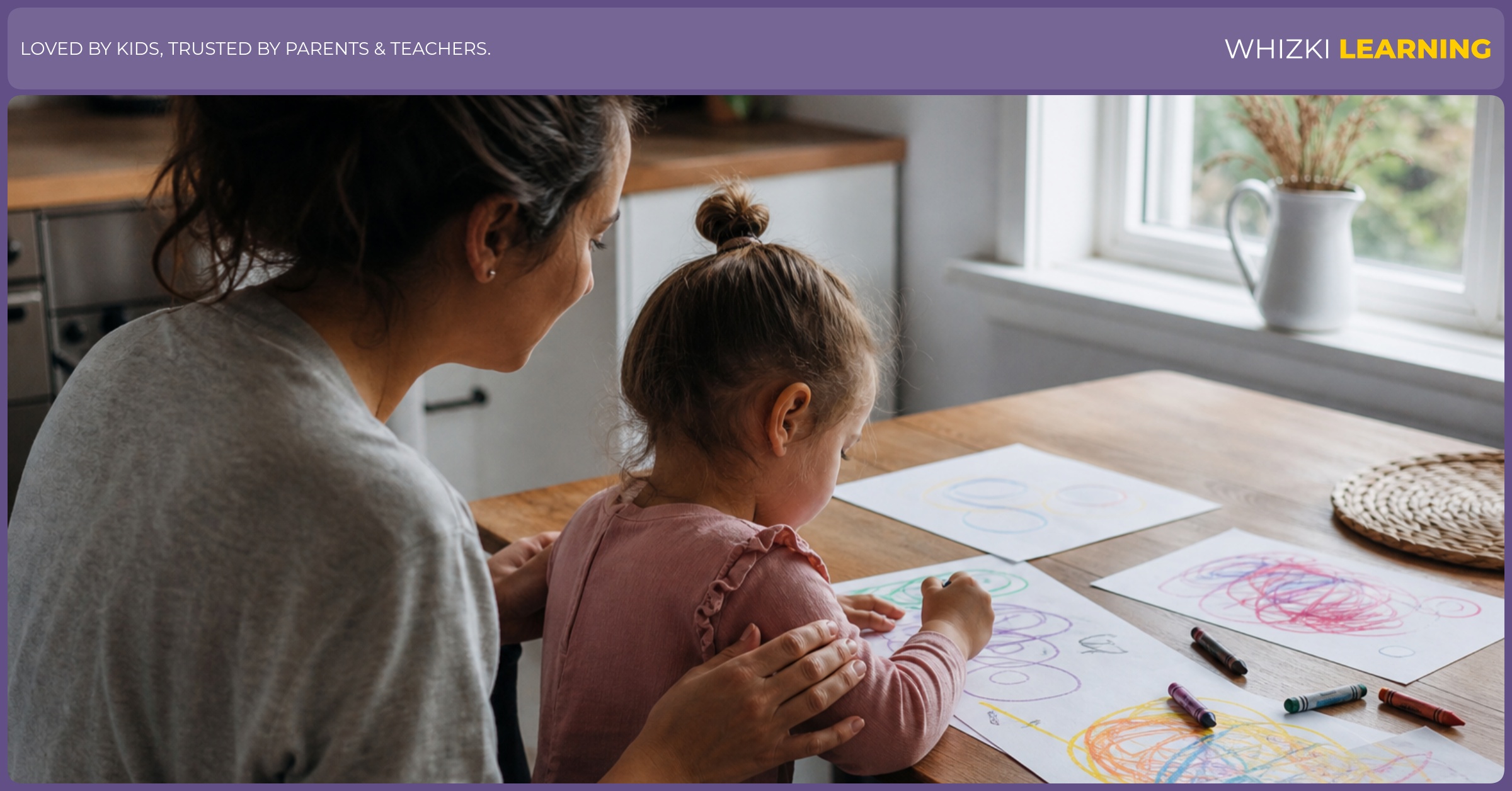 A parent sits beside a young child who is drawing with crayons at a kitchen table.