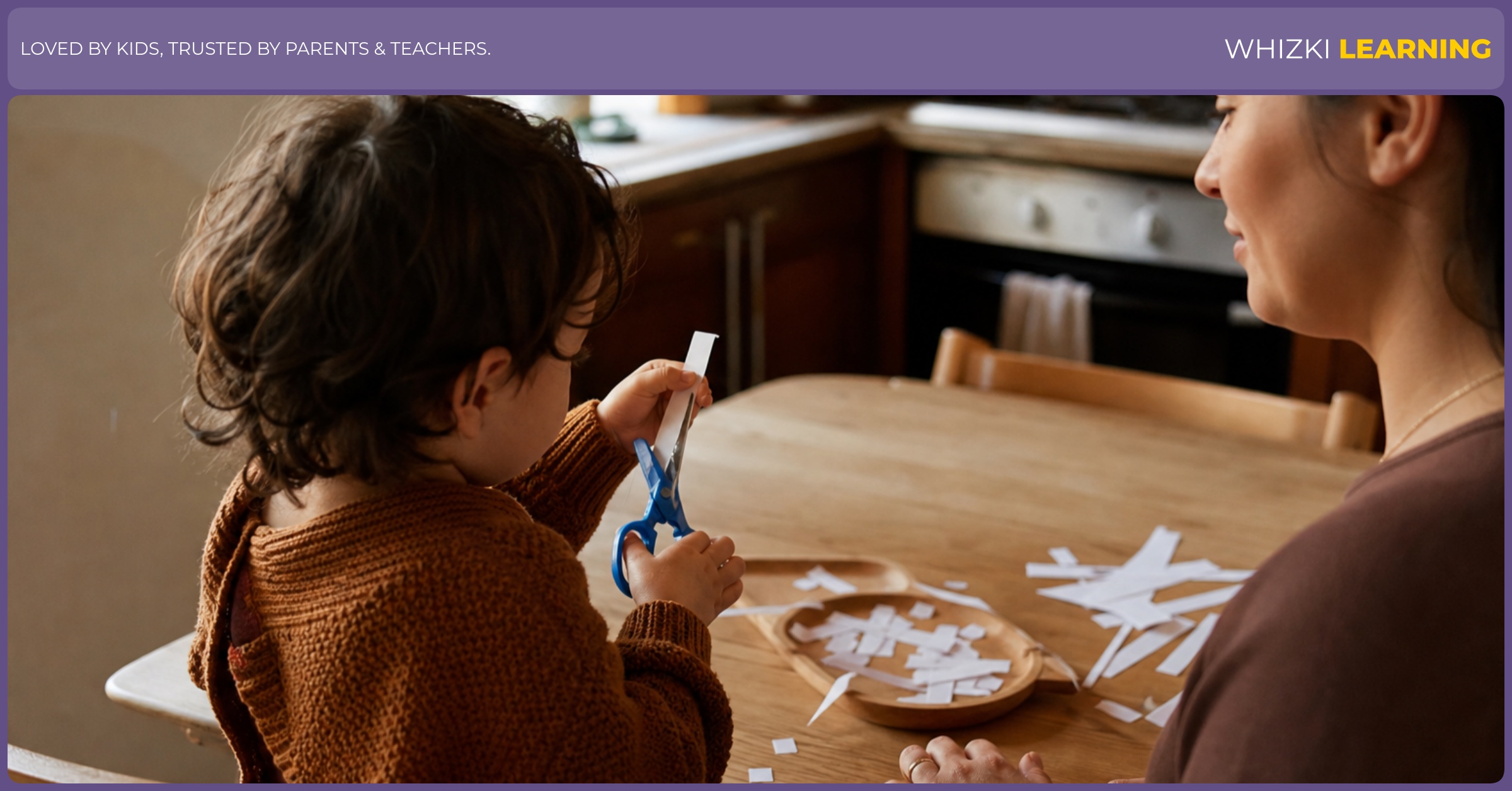 A parent sits beside a young child who is safely snipping narrow paper strips at a kitchen table.