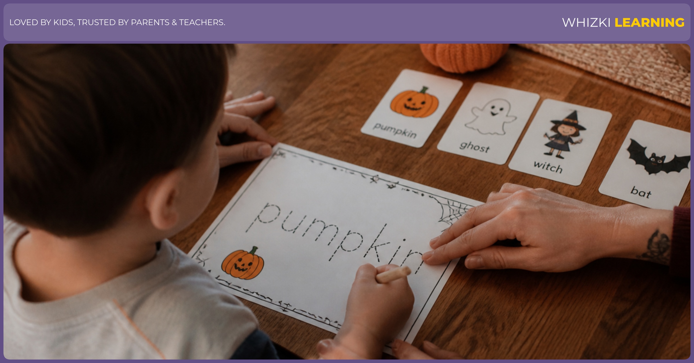 A child traces a Halloween word while a parent gently supports pencil grip at the kitchen table.