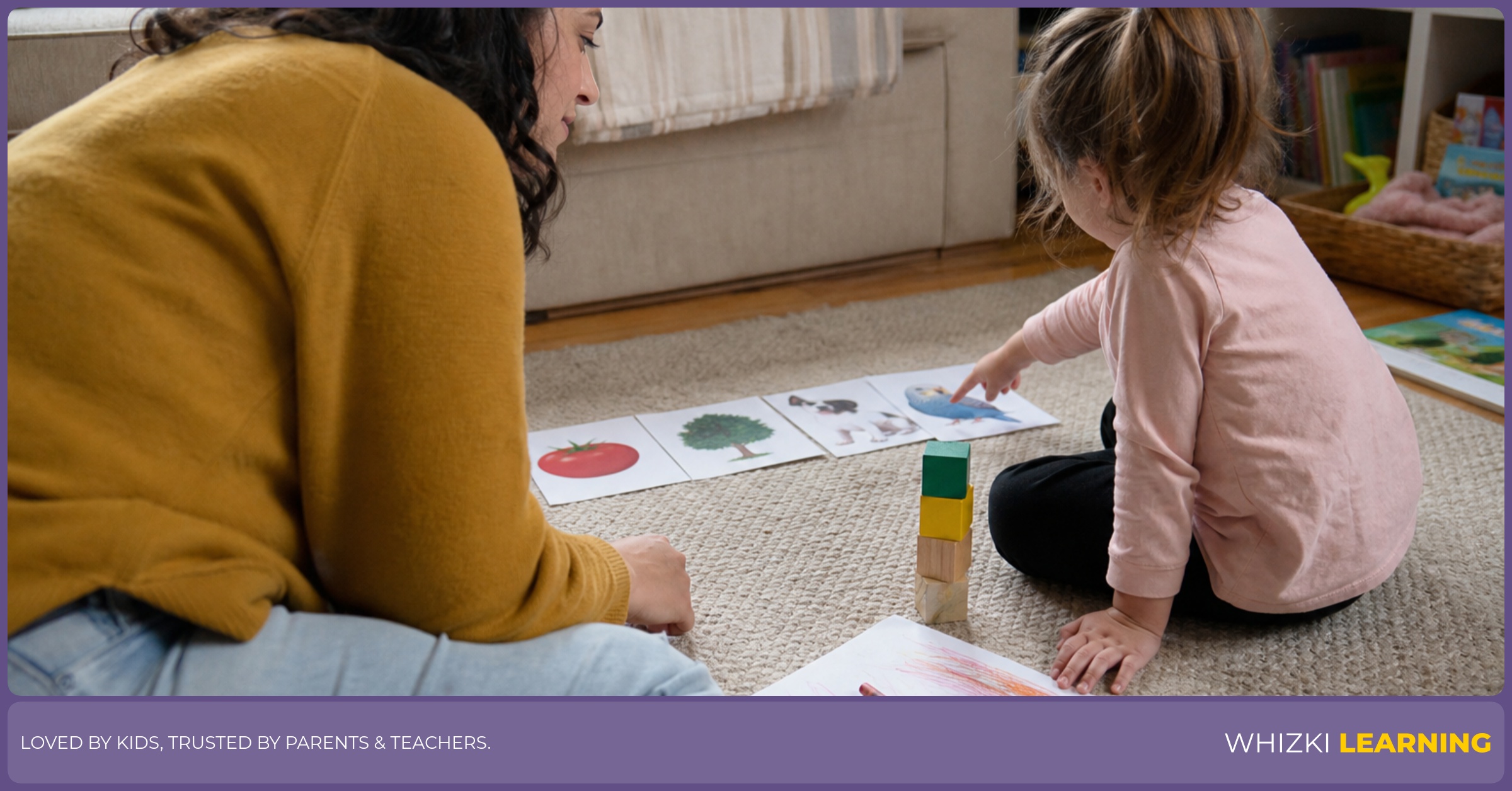 A caregiver watches a child point to picture cards and draw with crayons during a calm home-language activity.
