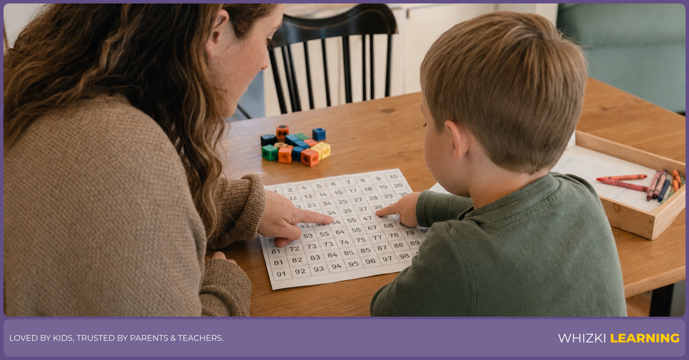 A parent points beside a child who follows a paper 100 chart at the kitchen table.
