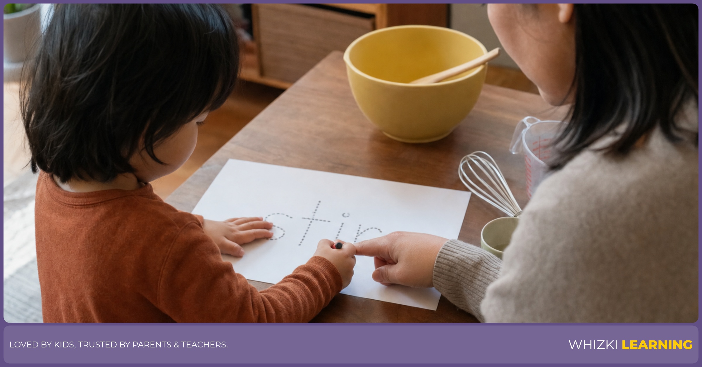 A caregiver helps a child trace a J verb word on paper at a kitchen table.
