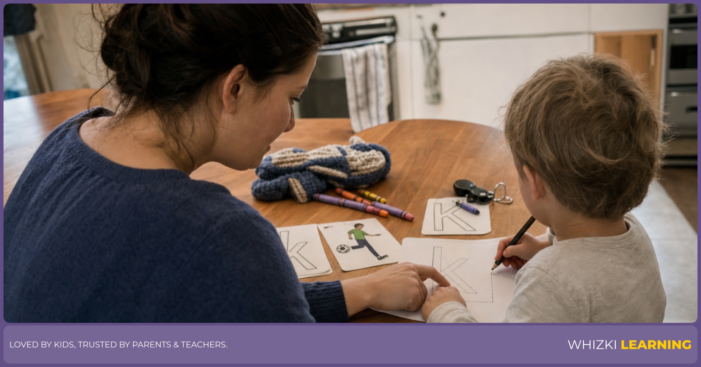 A caregiver helps a child trace K verb words on a printable at a kitchen table.