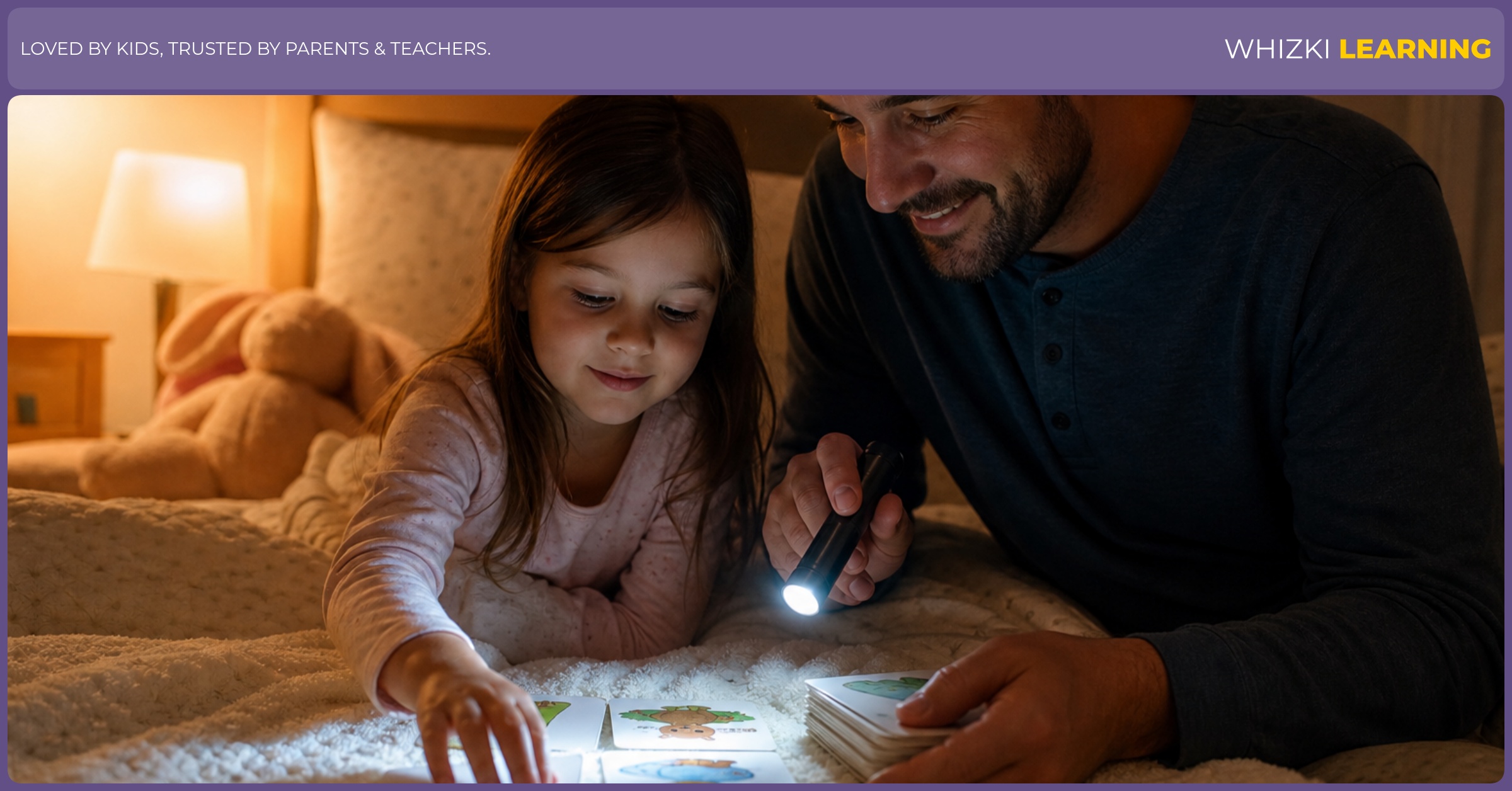 A parent and child sit on a bed with a small flashlight, shining it on picture cards labeled with K words while speaking softly. The room is warmly lit, and both look relaxed and engaged.