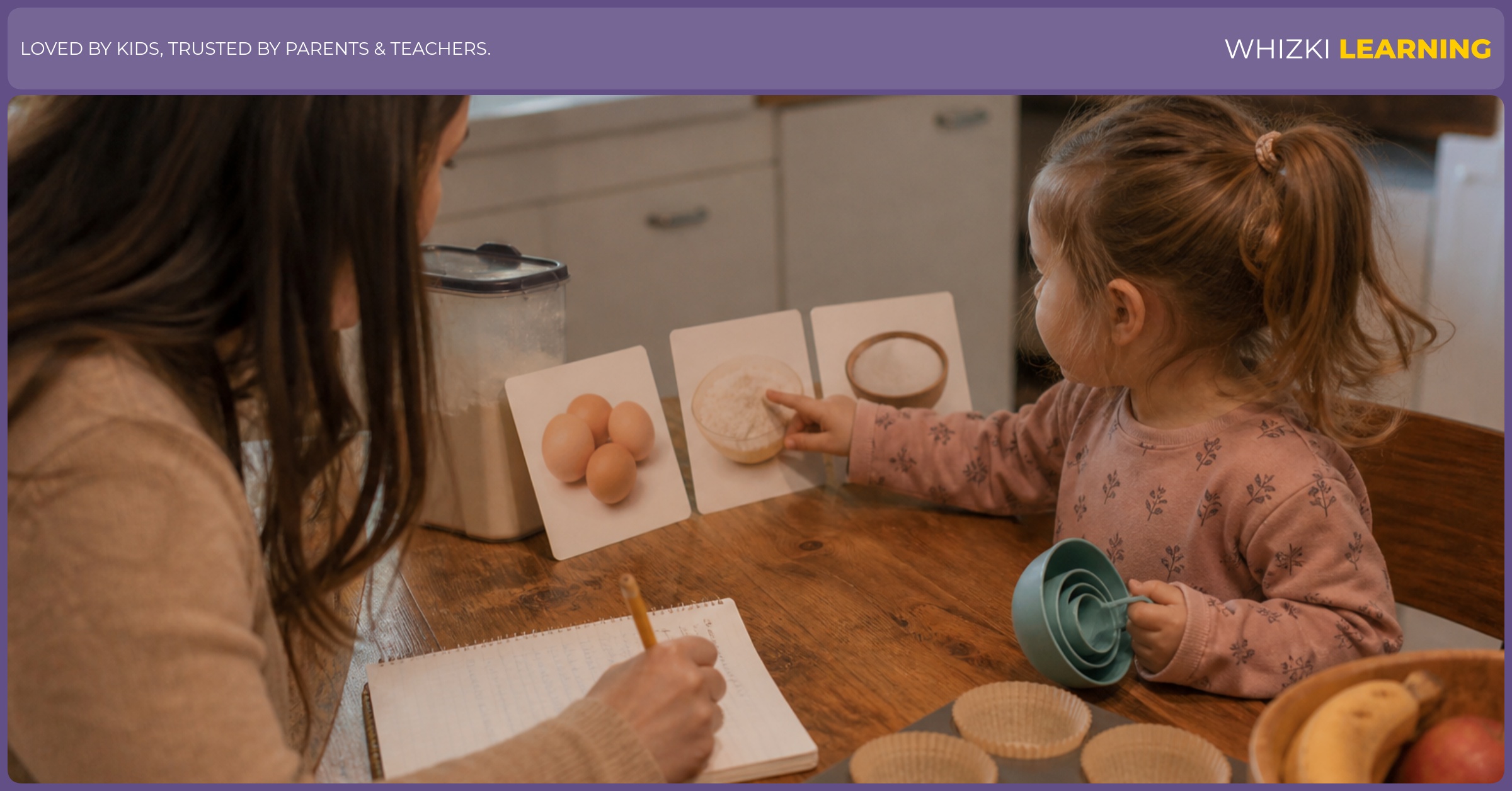 A parent writes a simple learning note while a young child uses measuring cups at a kitchen table.