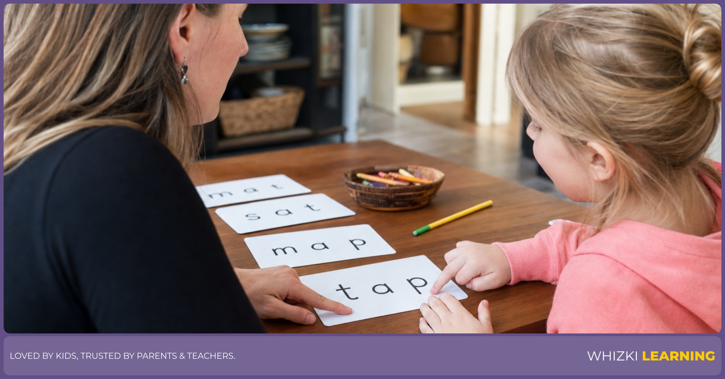 A parent helps a young child tap fingers while reading a CVC word card at the kitchen table.