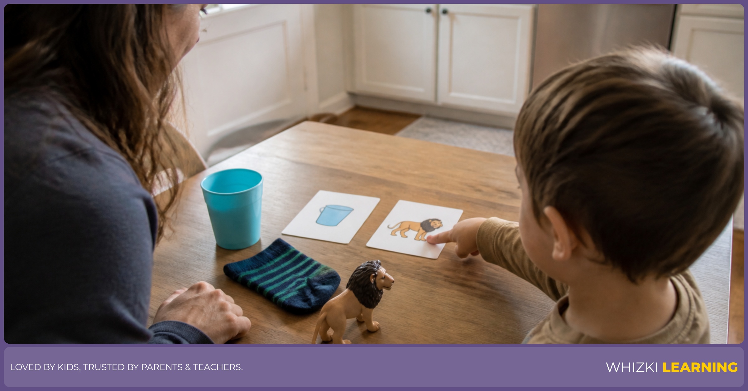 A parent and young child use two picture cards and real objects for a pointing choice at the kitchen table.