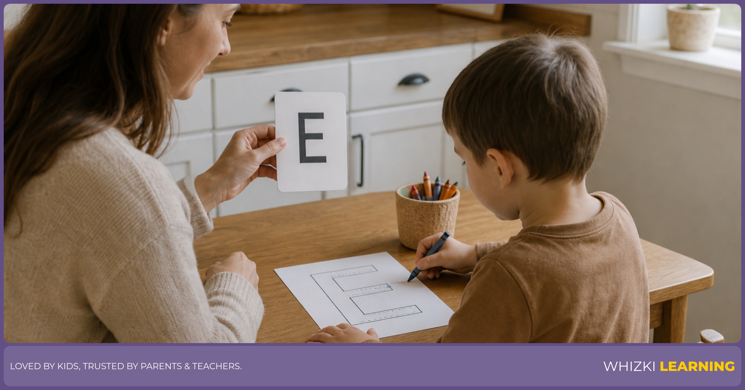 Parent and child practicing the letter E at a kitchen desk with a crayon, pointing to a card and saying an E adjective in a calm, focused moment