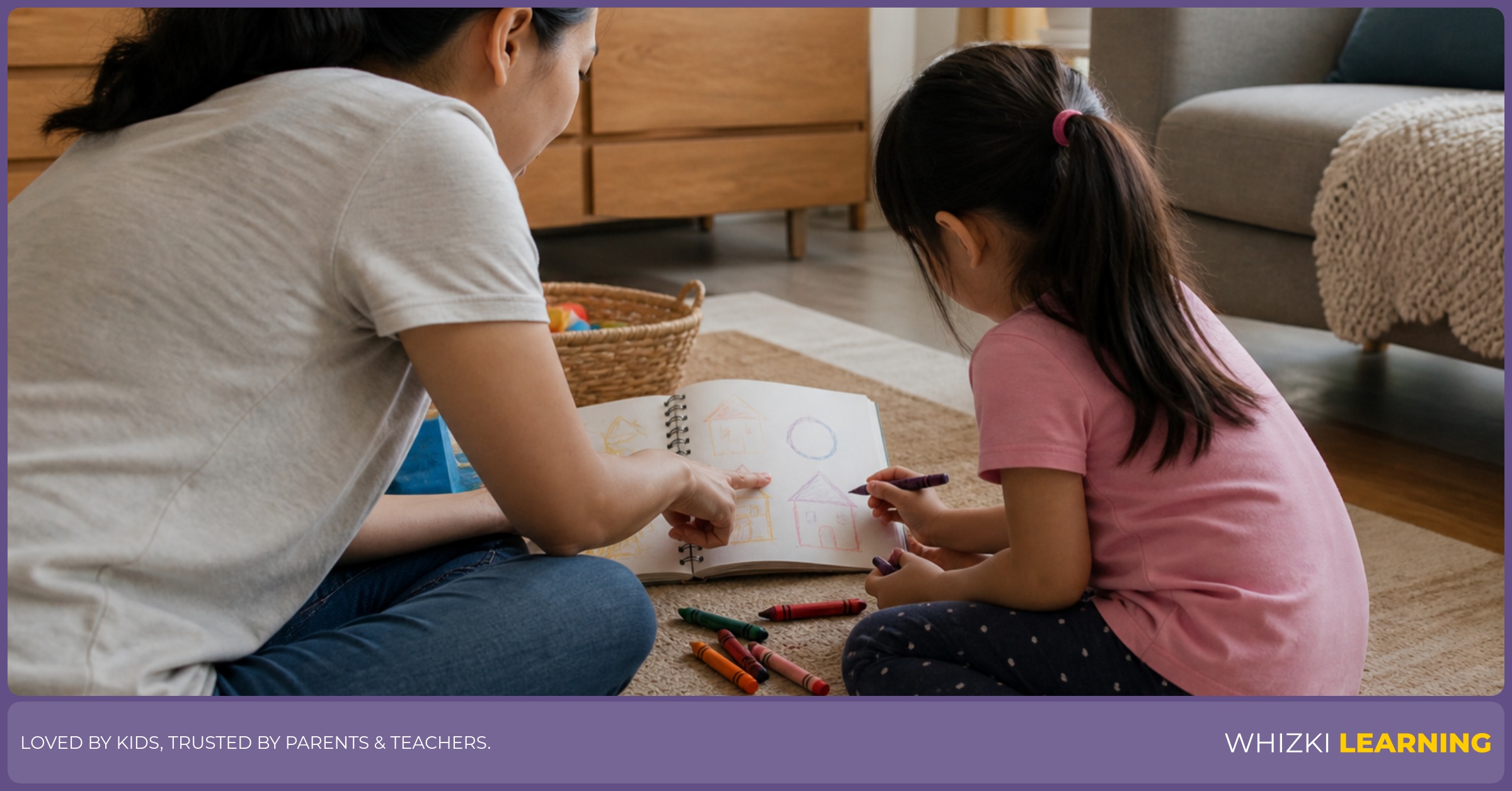 A caregiver sits on a living-room rug with a child who is drawing shapes on paper beside a picture book.