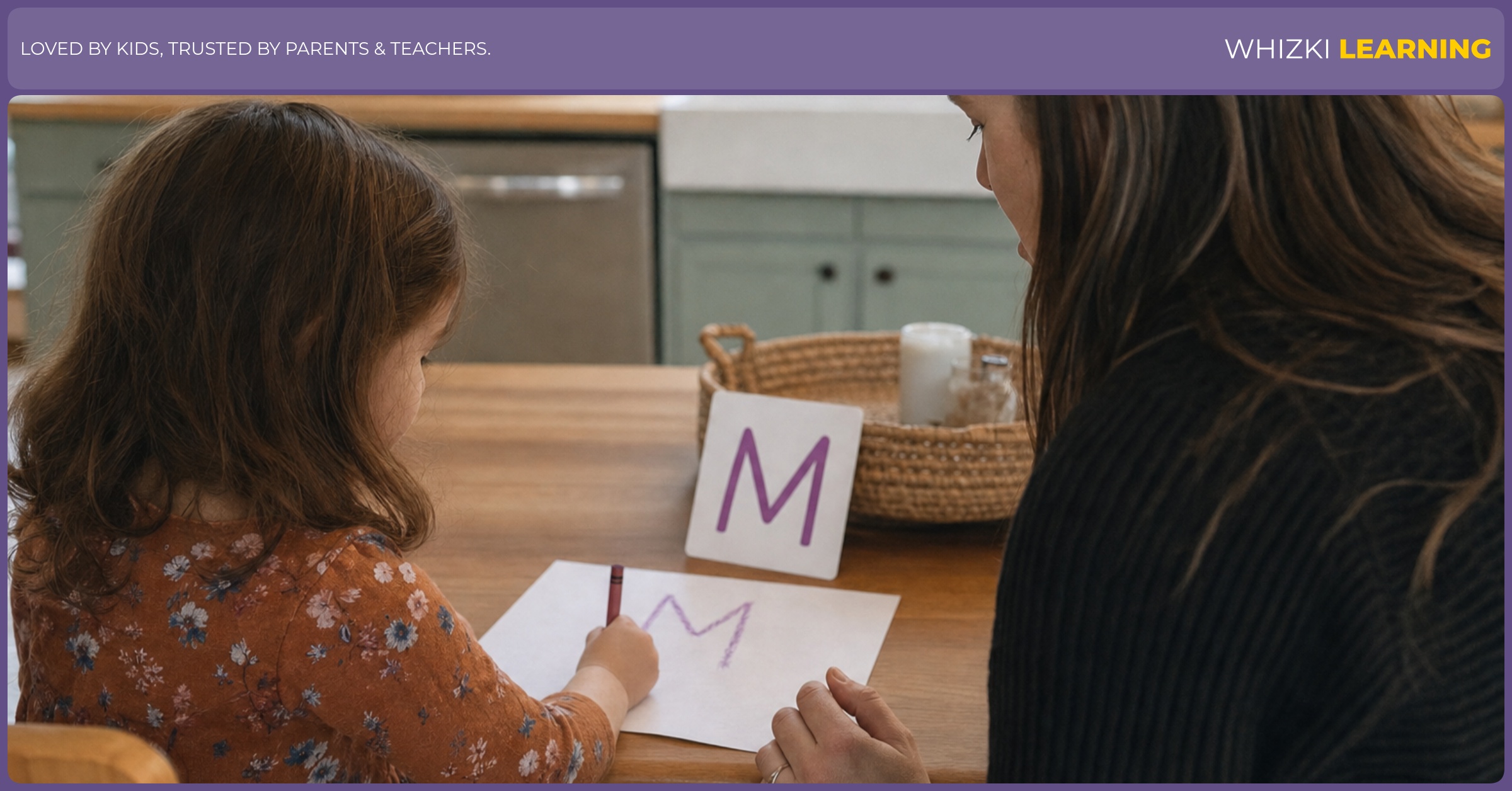 A parent sits beside a preschool child at a kitchen table while the child practices the first letter of their name with a crayon.