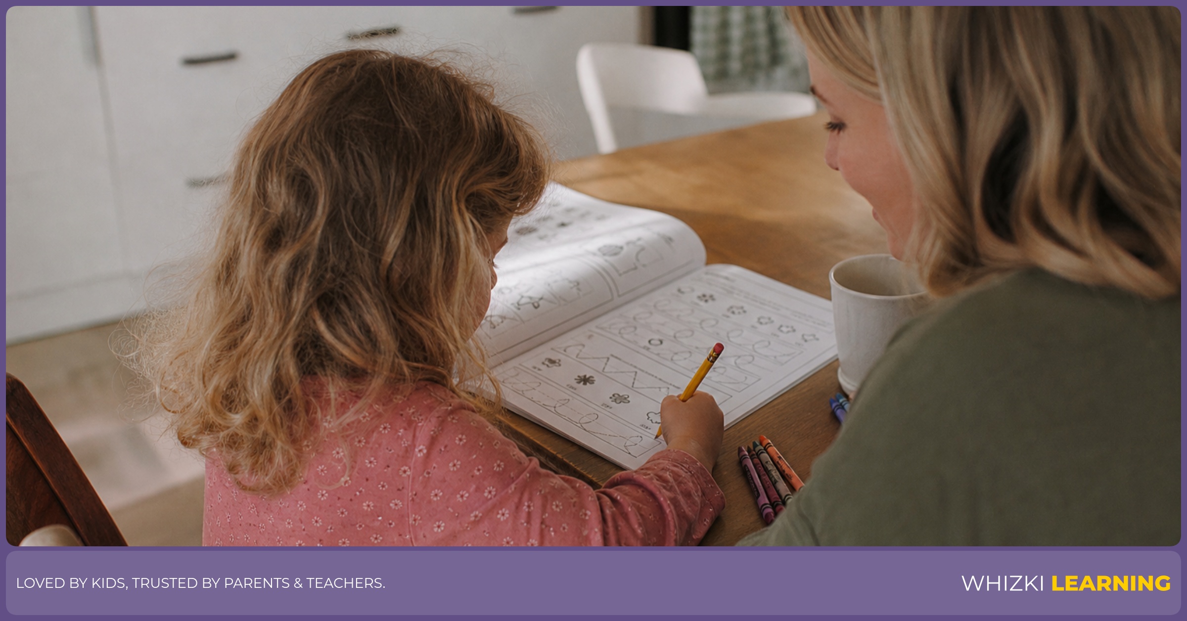 A parent sits beside a child practicing pencil strokes in a printed workbook at a kitchen table.