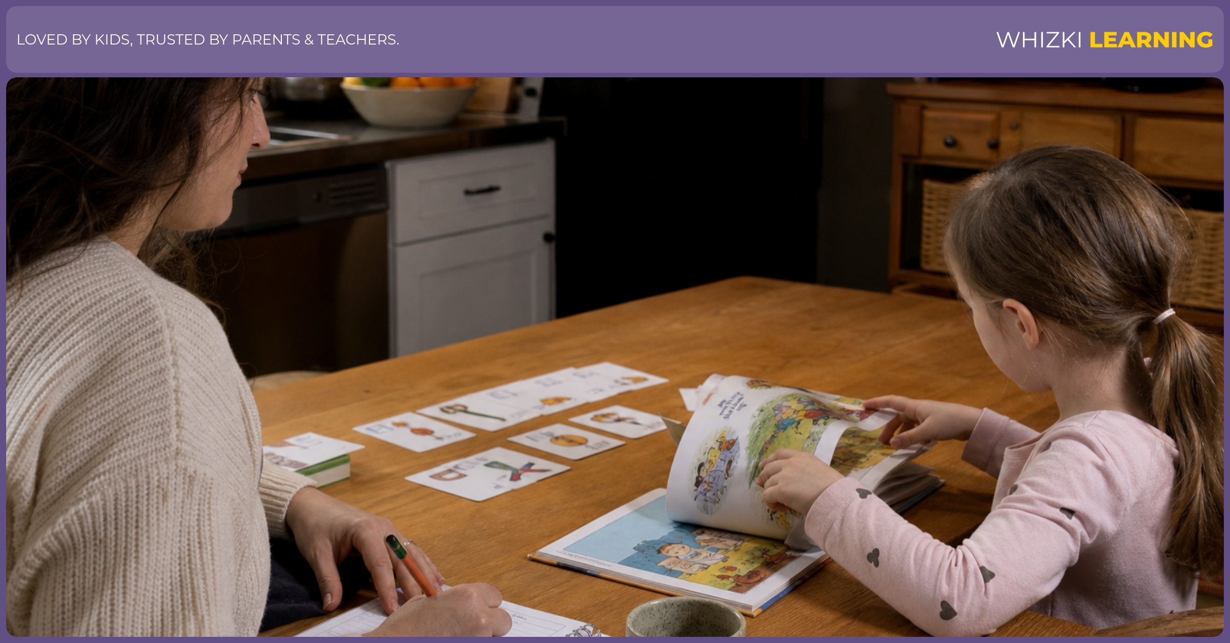 A parent writes a short reading note while a child turns pages in a picture book at the kitchen table.