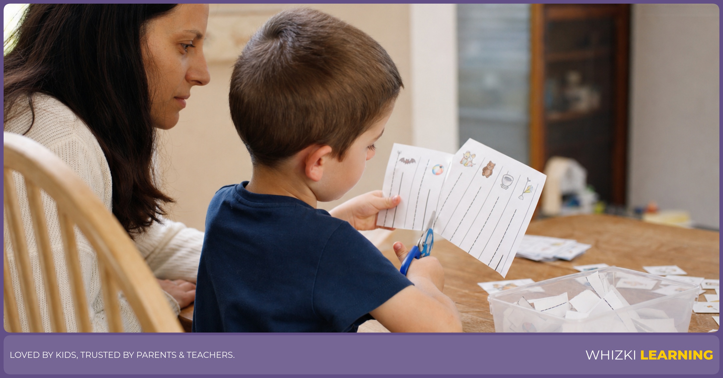 A parent sits beside a preschool child practicing short straight-line cuts on a worksheet at the kitchen table.