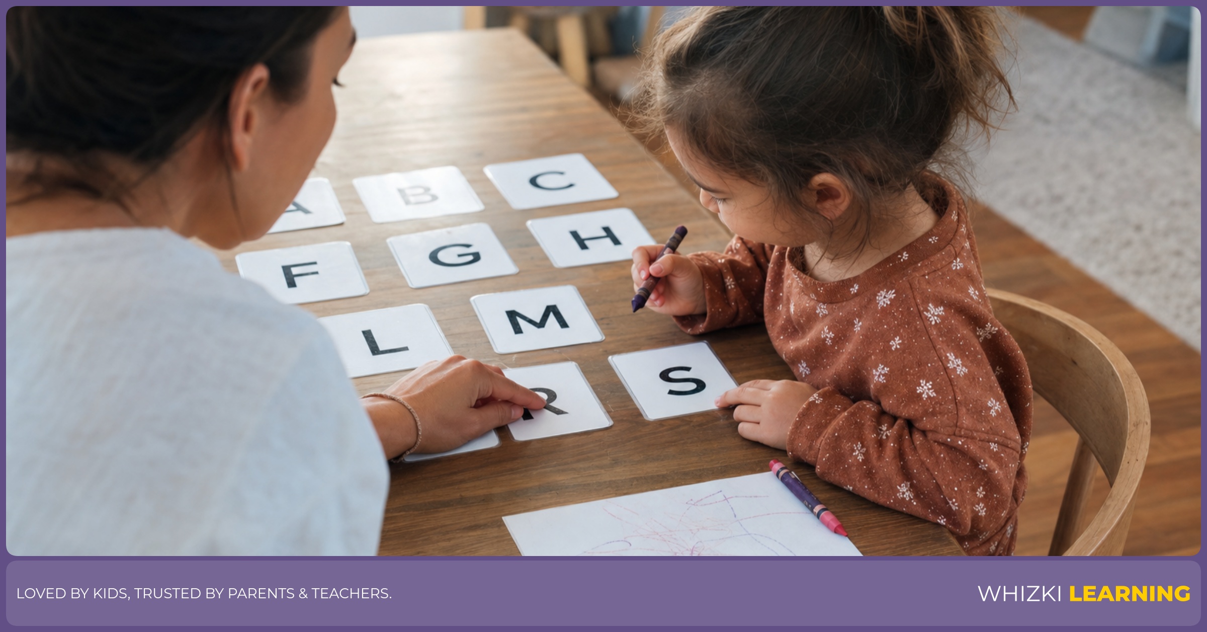 A parent helps a young child match uppercase letter cards at a kitchen table with crayons nearby.