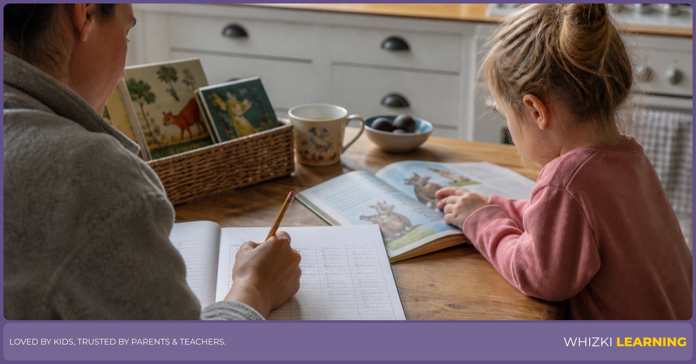 A parent writes in a reading log while a young child looks at a picture book at the kitchen table.