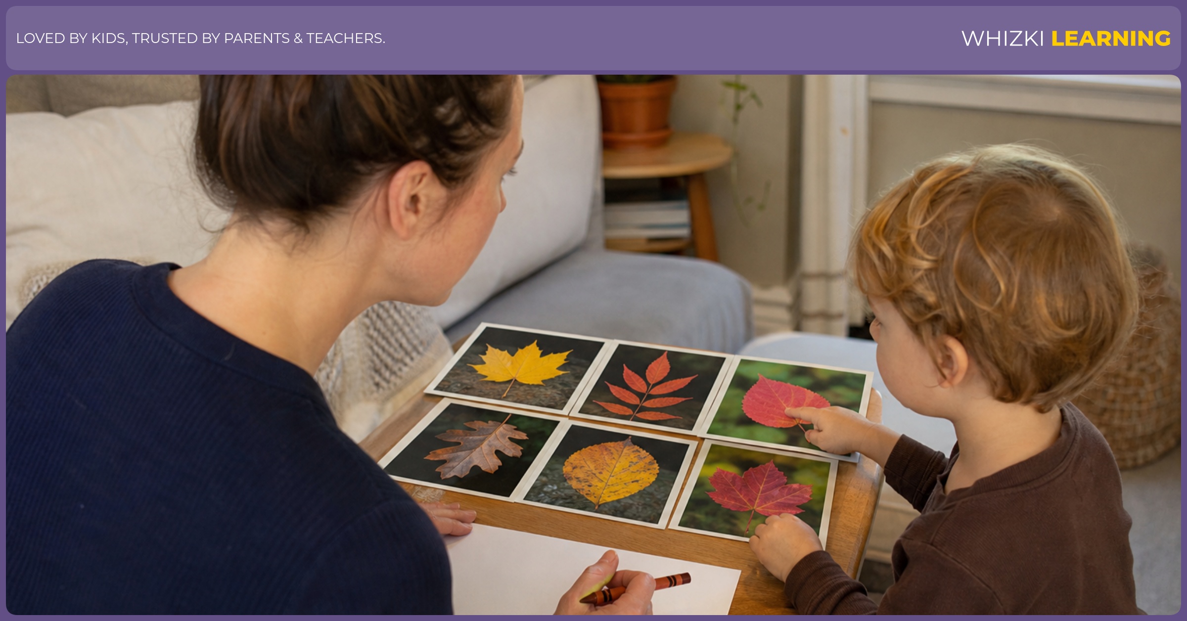 A caregiver and child compare printed photos of leaves at a living room table with crayons nearby.