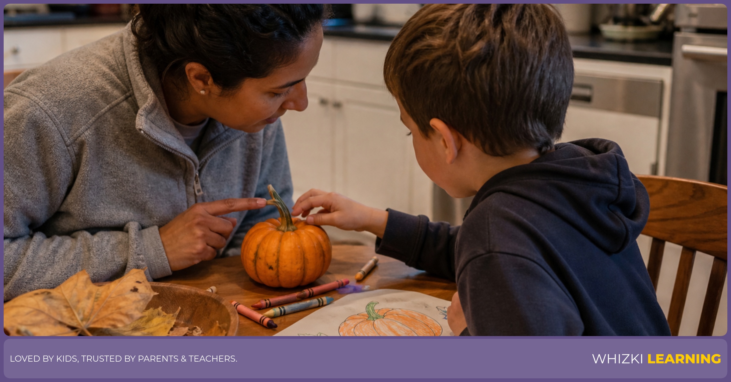 A caregiver and child study a small pumpkin at a kitchen table with crayons, paper, and leaves nearby.