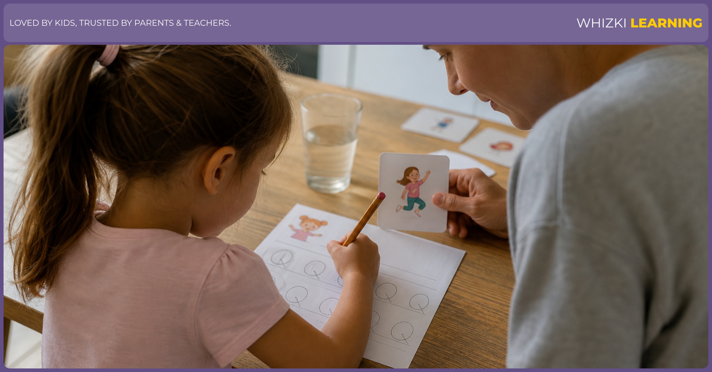 A caregiver guides a child's pencil grip while the child traces Q action words at a kitchen table.