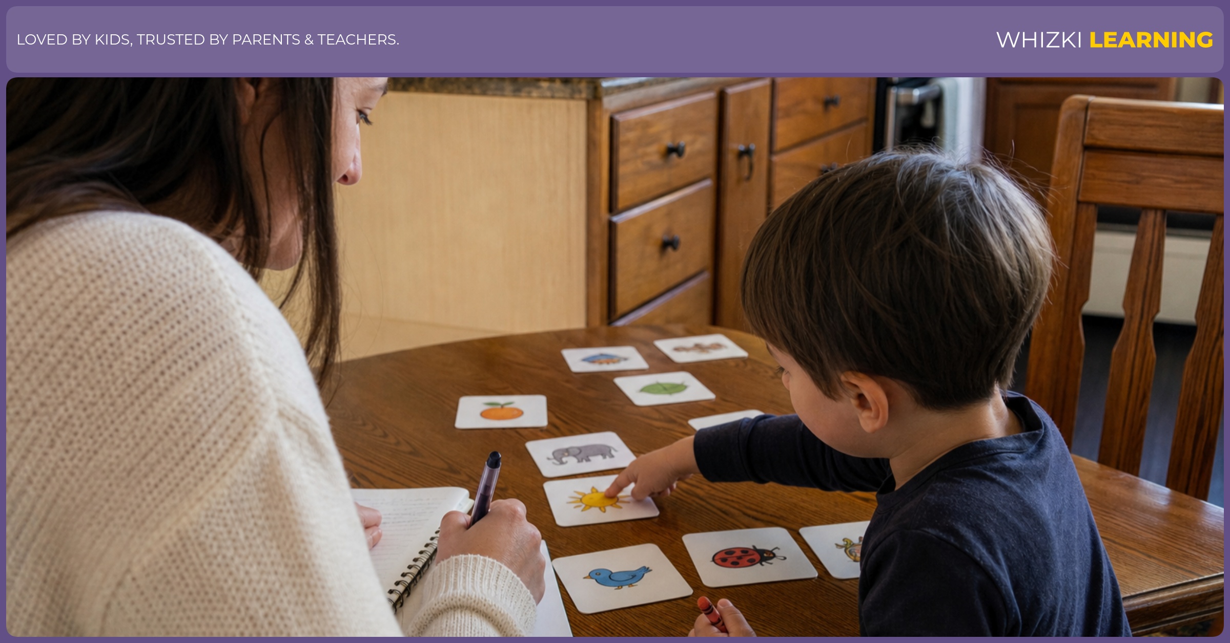 A parent writes home-language notes while a young child points to picture cards at the kitchen table.