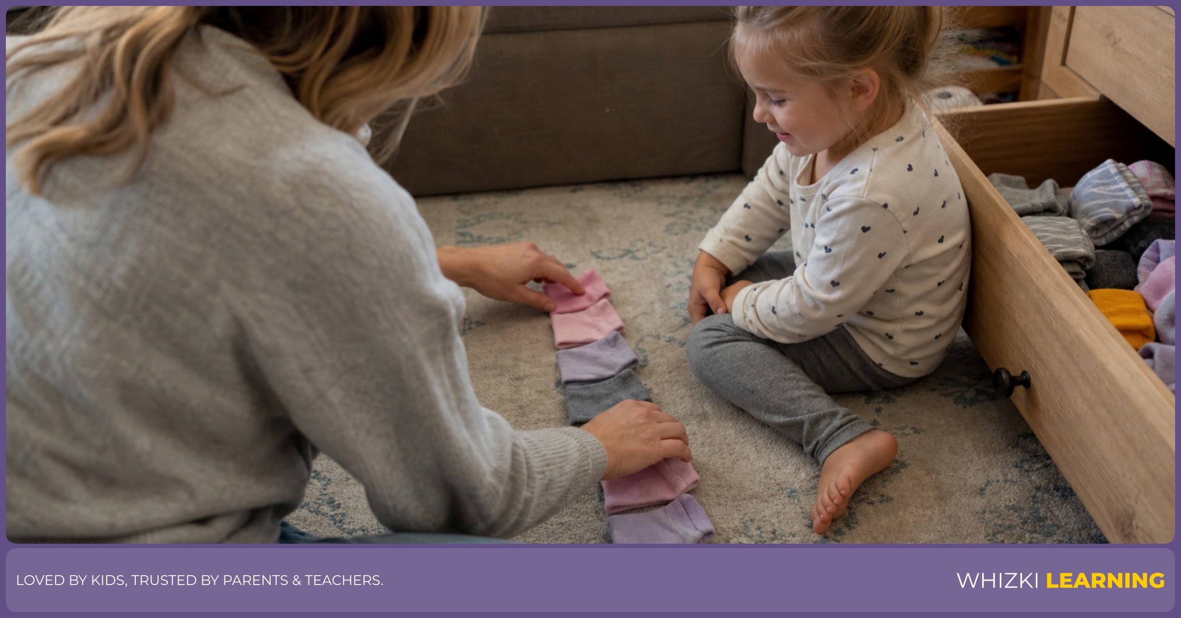 A caregiver and young child sit on a rug arranging socks into a red and blue repeating pattern.