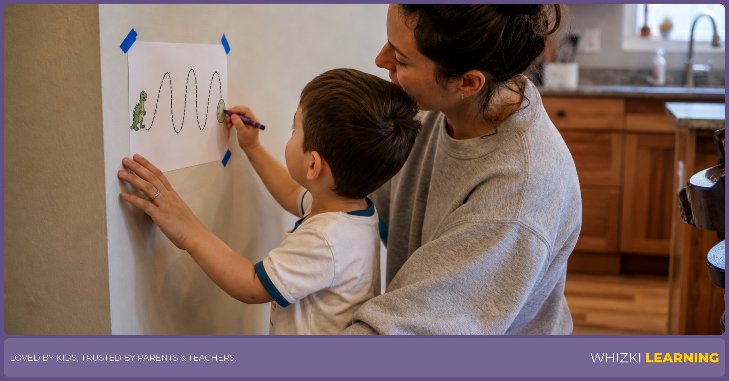 A caregiver tapes a worksheet to the wall while a preschool child traces with a crayon.