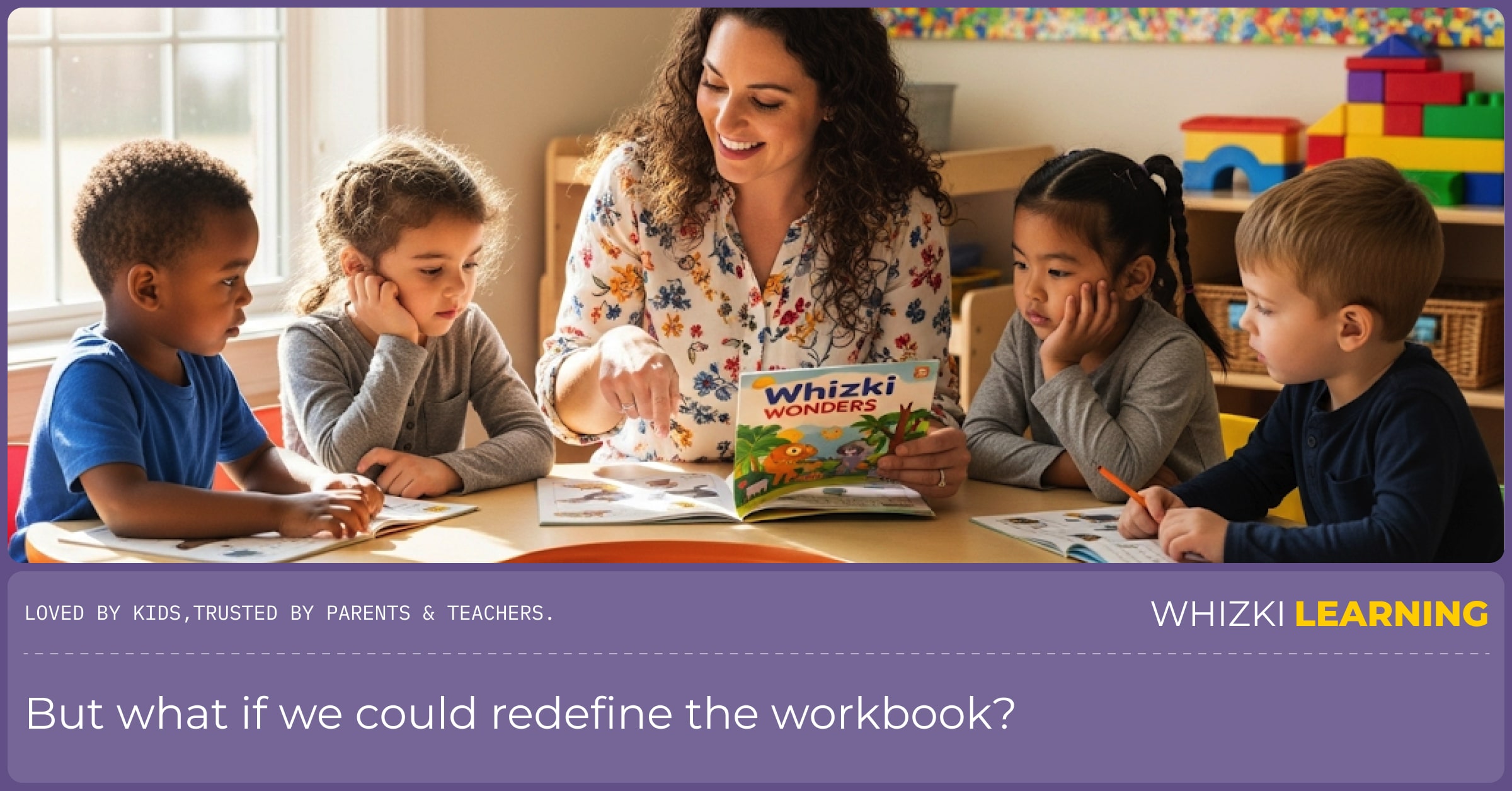 A female teacher sits at a small table with three young students. They are smiling and looking at the open workbooks in front of them.