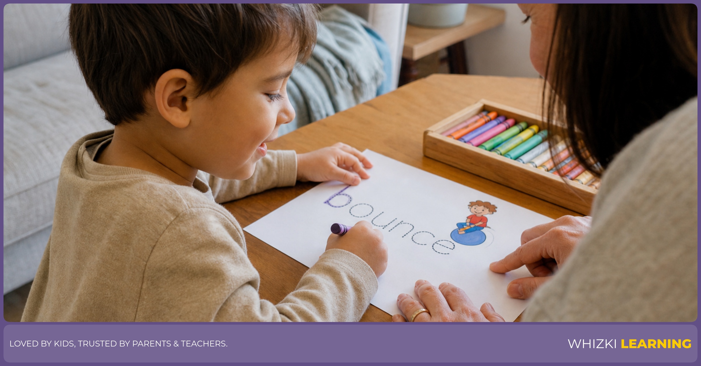 A child traces a B action word with a crayon while a parent guides the paper from the side.