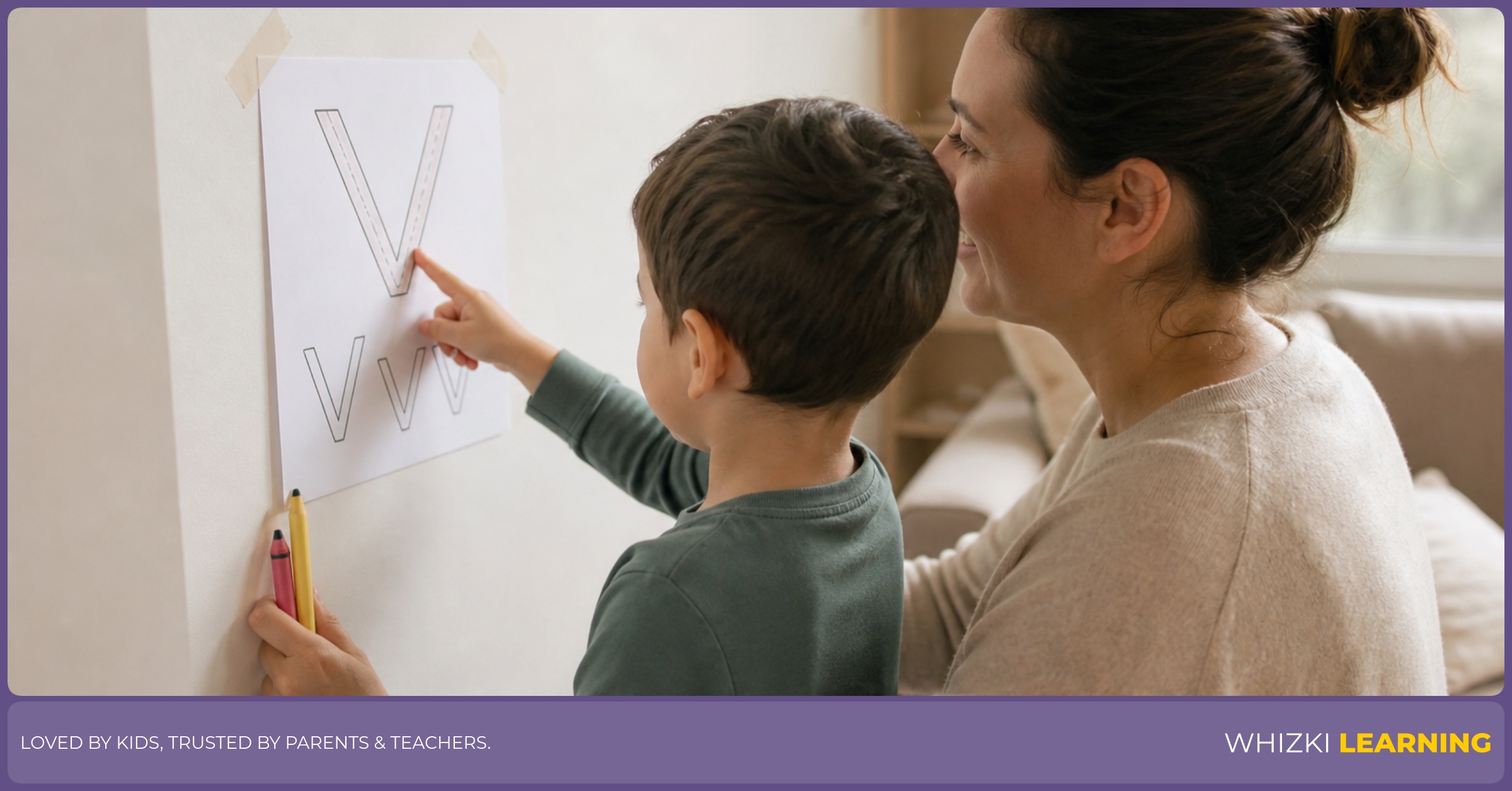 A caregiver helps a child trace V words on a printable taped to a wall.