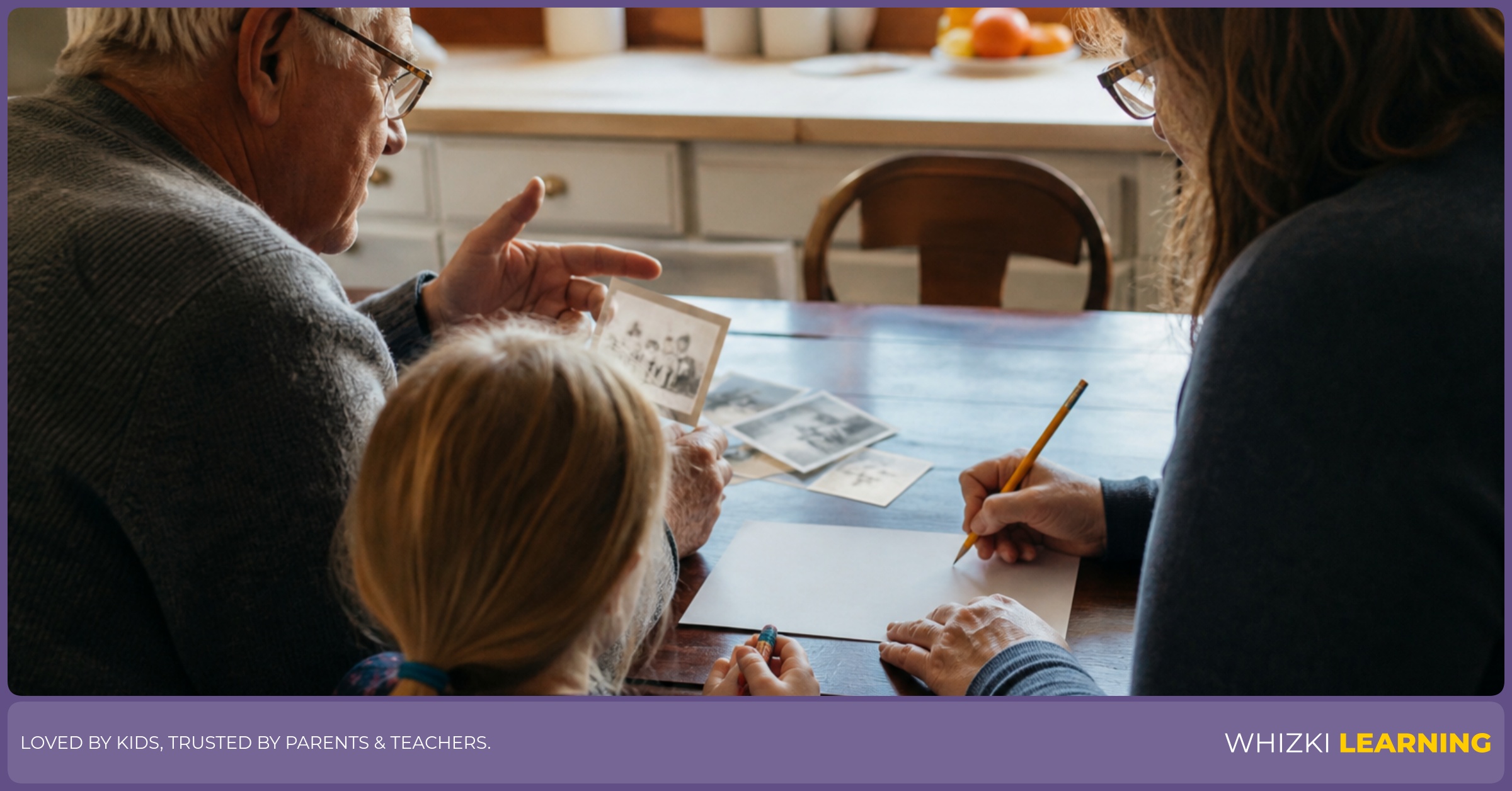 A grandparent, parent, and young child sit at a kitchen table making a bilingual story page with paper, pencil, and crayons.