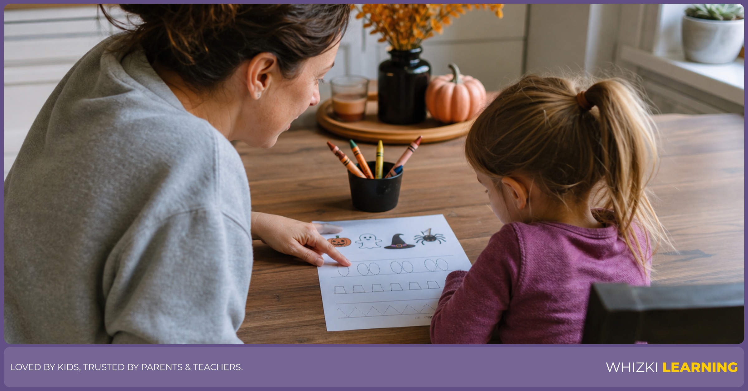 A caregiver and child preview a Halloween worksheet together at a kitchen table before writing.
