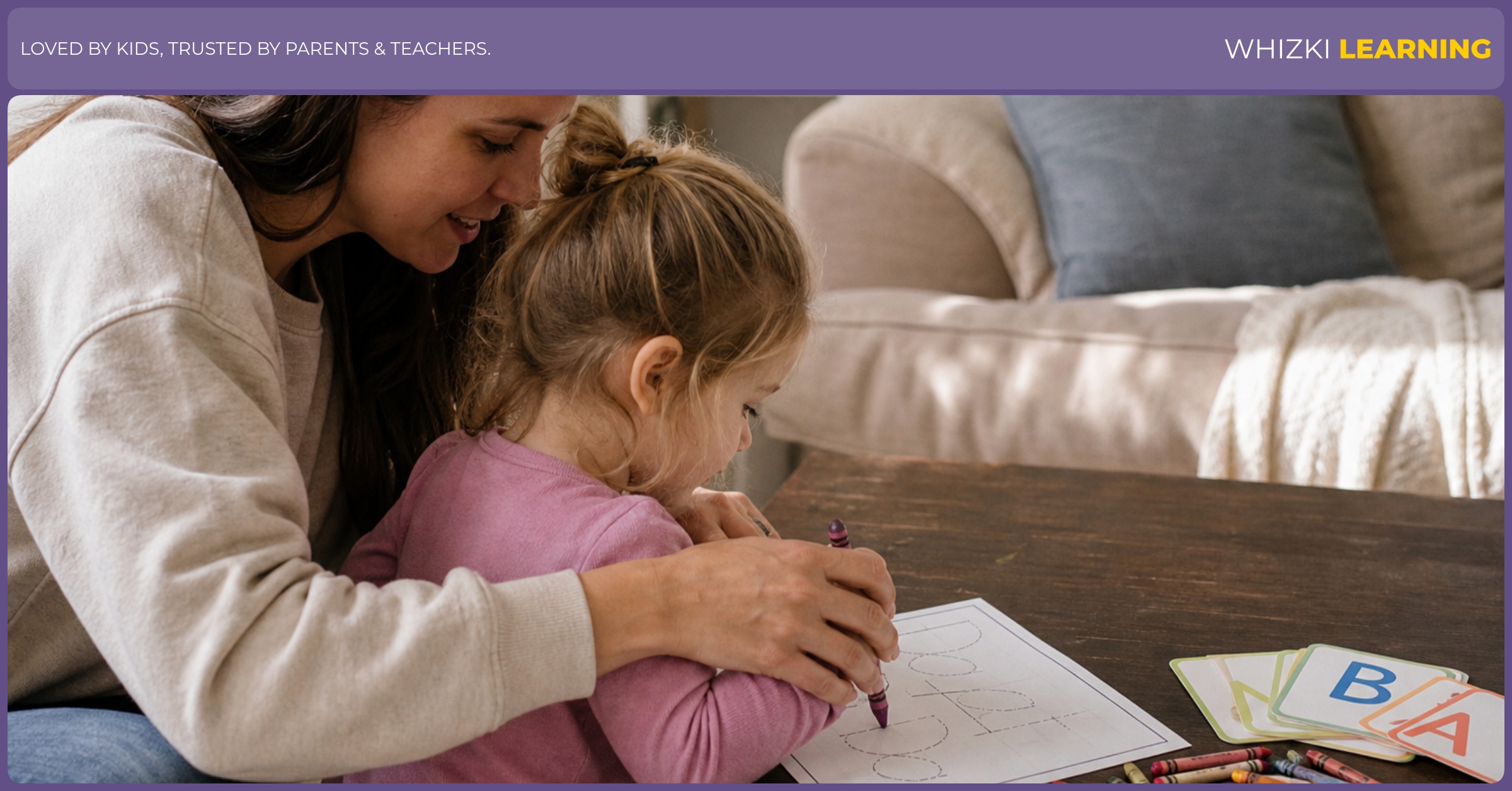A parent helps a child trace a simple name page with a thick crayon on a low living-room table.
